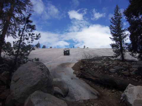 1968 Ford Bronco - A vehicle navigates a challenging snowy incline under a bright blue sky with scattered clouds.