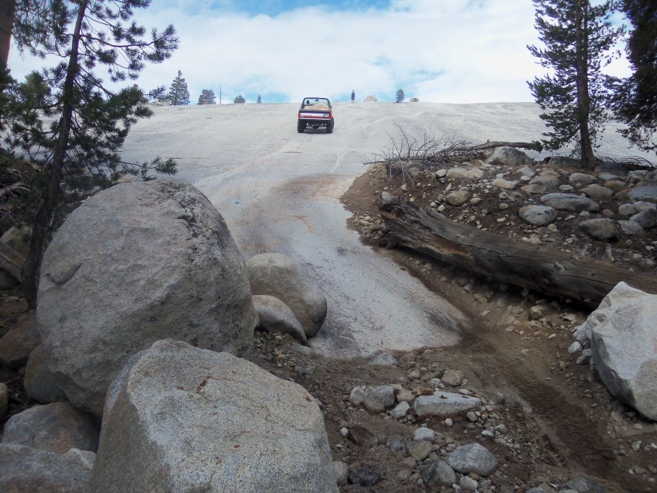 Red SUV driving up a snowy hill with large rocks in the foreground