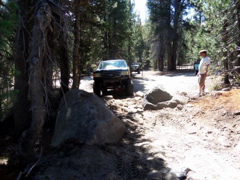 1968 Ford Bronco - Off-road vehicles traverse a challenging, rocky path through a forest with a person observing.