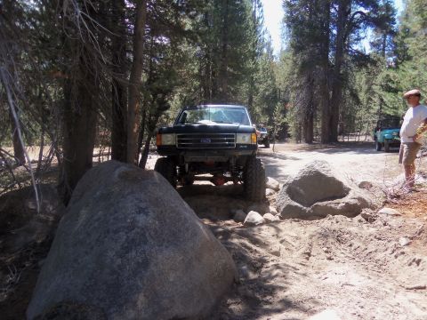 1968 Ford Bronco - A black Ford Bronco navigates a rocky, wooded trail with another vehicle visible in the background.