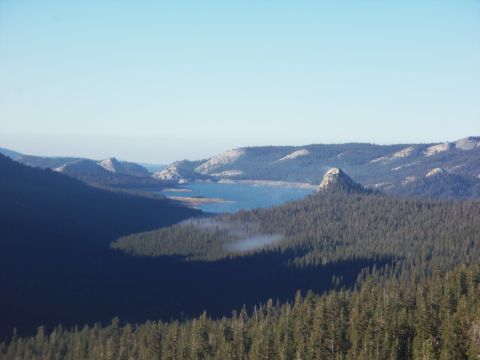 1968 Ford Bronco - Scenic landscape of a pine-forested mountain valley with a distant reservoir and rocky domes under clear blue sky.