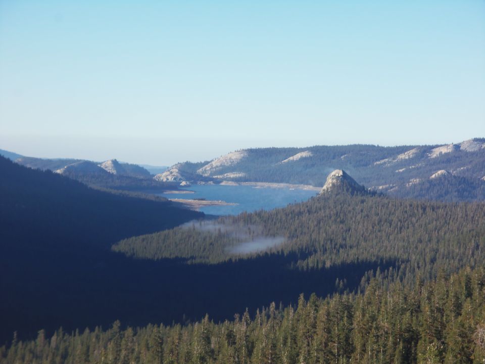 Forested mountain valley with reservoir and morning haze under blue sky