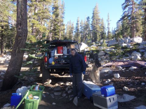 1968 Ford Bronco - A man stands by a green Ford F-Series pickup truck loaded with camping equipment in a wooded, rocky area.