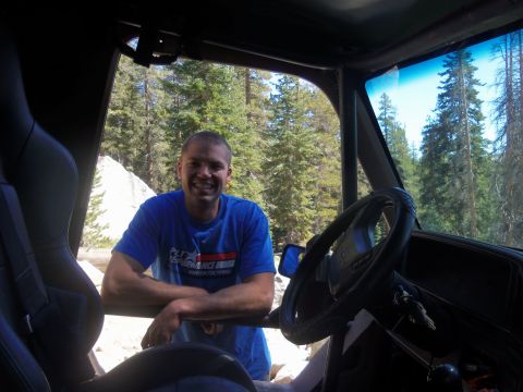 1968 Ford Bronco - Man poses inside a modified off-road vehicle, with a forest and rocky terrain visible through the open door.