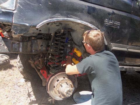 1968 Ford Bronco - A mechanic works on the suspension system of a black SUV, focusing on the coil spring and brake assembly.