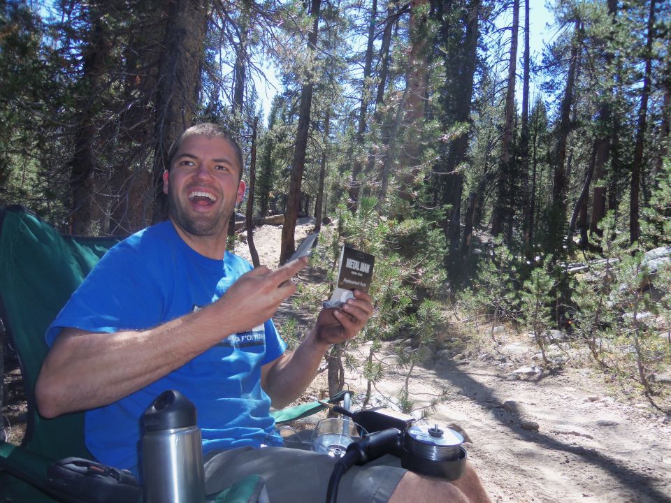 Man in blue shirt holding a box labeled "MERLIN" in a forest setting