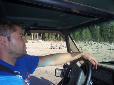 1968 Ford Bronco - Driver's perspective inside an off-road vehicle on a dirt path with trees in the background.