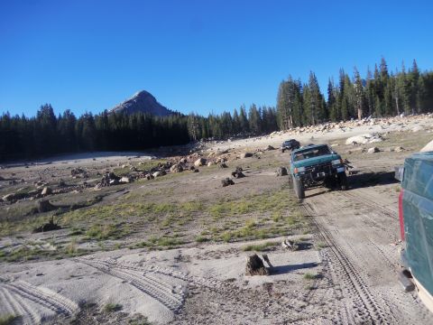 1968 Ford Bronco - Several off-road vehicles navigate a dusty trail in a rocky, mountainous landscape under a clear blue sky.