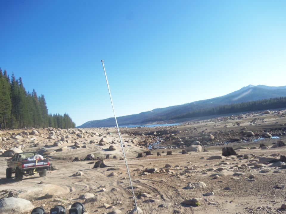 Red 1968 Ford Bronco parked on rocky terrain with trees and a lake in the background