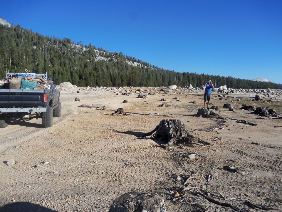 Truck loaded with lumber and debris parked on dirt road in deforested area with a person standing in the distance