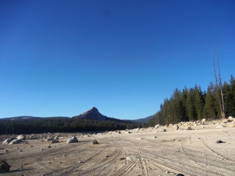 1968 Ford Bronco - A wide, arid landscape features tire tracks across the dusty ground, with a prominent mountain peak in the distance.