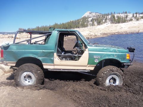 1968 Ford Bronco - This modified Bronco is deep in the mud near a body of water, with a roll cage and no doors.