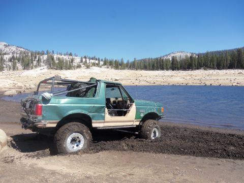 1968 Ford Bronco - A modified Ford Bronco is partially submerged in mud near the edge of a body of water under a clear blue sky.