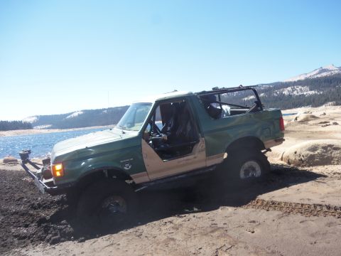 1968 Ford Bronco - Off-road SUV with doors removed is stuck in the mud next to a body of water.