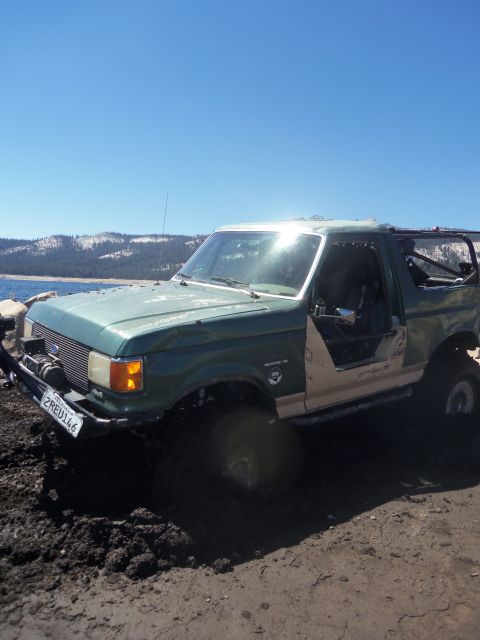 1968 Ford Bronco - This modified Ford Bronco is stuck in the mud next to a body of water with mountains in the background.