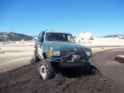1968 Ford Bronco - This modified truck appears to be stuck in a muddy off-road area, a winch and auxiliary lights on the front bumper.