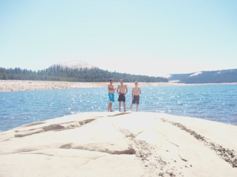 1968 Ford Bronco - Three young men on a rocky shore by a lake with a mountain in the distance.