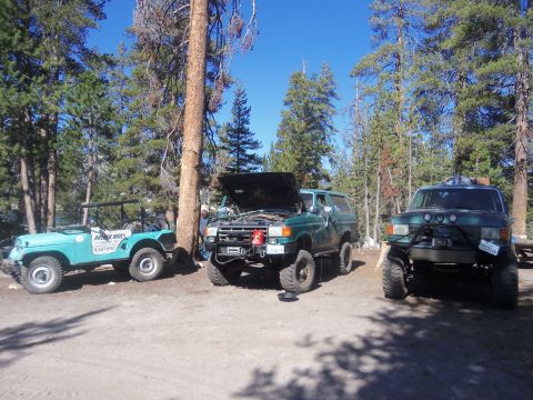1968 Ford Bronco - A trio of off-road vehicles are parked in a scenic, wooded location under a clear blue sky.
