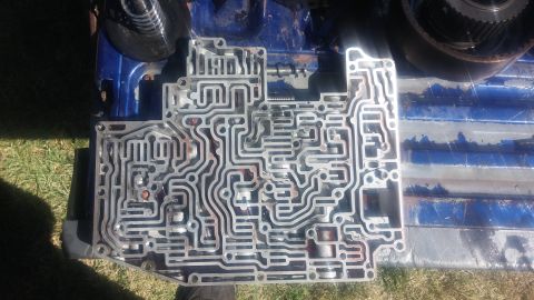 1986 Ford Bronco - This intricate metal component, a transmission valve body, is laid out on a blue surface, possibly a truck bed.