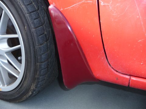 1993 Mazda MX-3 - Close-up of a red car's side panel, showing a mud flap and wheel.