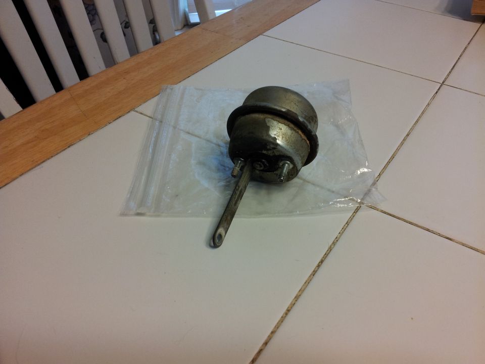 Metal vacuum actuator with a rod, resting on a plastic bag on a tiled floor