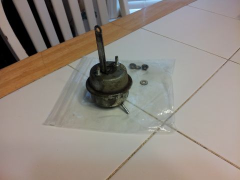 1976 Ford Ranchero - A vacuum actuator part with its lever and hardware is laid out on a tiled surface.