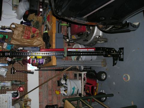 1996 Ford Bronco - A Hi-Lift Jack is positioned near the rear of a vehicle, with various tools and supplies visible in the background.