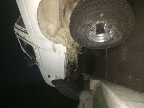 1994 Ford Bronco - White pickup truck appears to be a Ford Bronco, tilted on its side with large off-road tires.