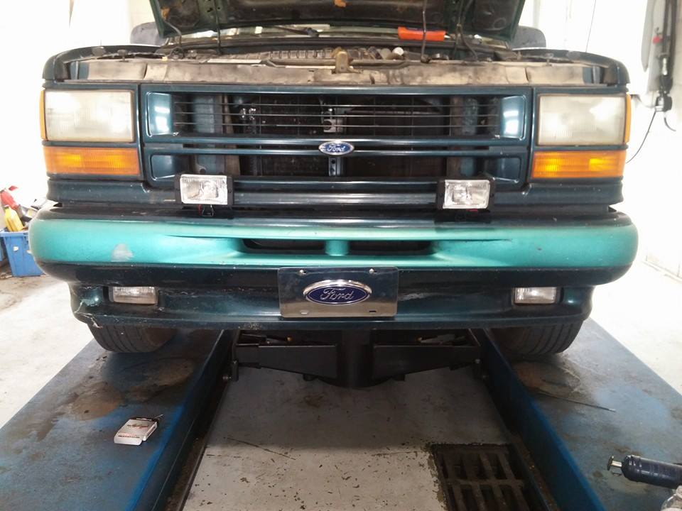 Green Ford Explorer front end with hood open, on a lift. Teal bumper, Ford grille emblem