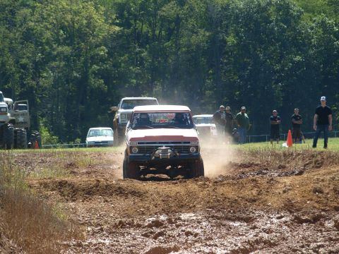1978 Ford Bronco - Multiple trucks navigate a muddy off-road course on a sunny day.