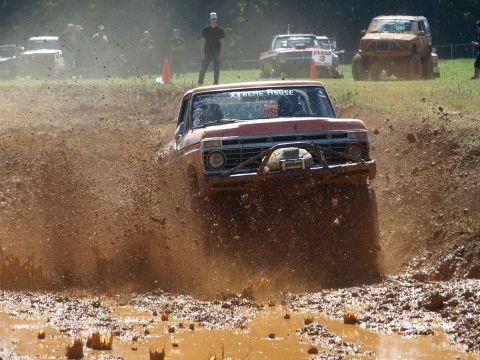 1978 Ford Bronco - A red pickup truck navigates a muddy obstacle course, kicking up a large spray of dirt and water.