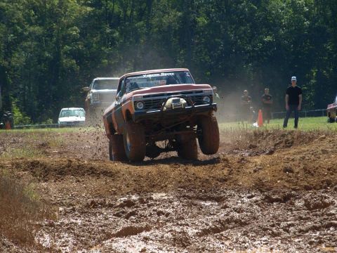 1978 Ford Bronco - This modified pickup truck is airborne during a mud bogging event, with other vehicles and spectators in the background.