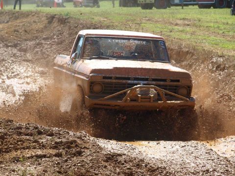 1978 Ford Bronco - This orange pickup truck is navigating a muddy obstacle course, kicking up a large spray of mud.