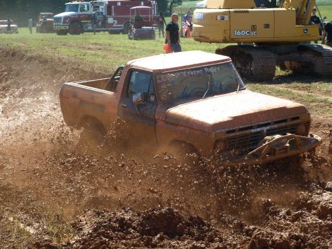 1978 Ford Bronco - This orange pickup truck is deep in the mud, with 'Xtreme Rules' visible on its windshield.