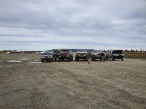 1990 Ford F-250 - Several modified trucks are gathered in an outdoor lot, with a few people standing around them.