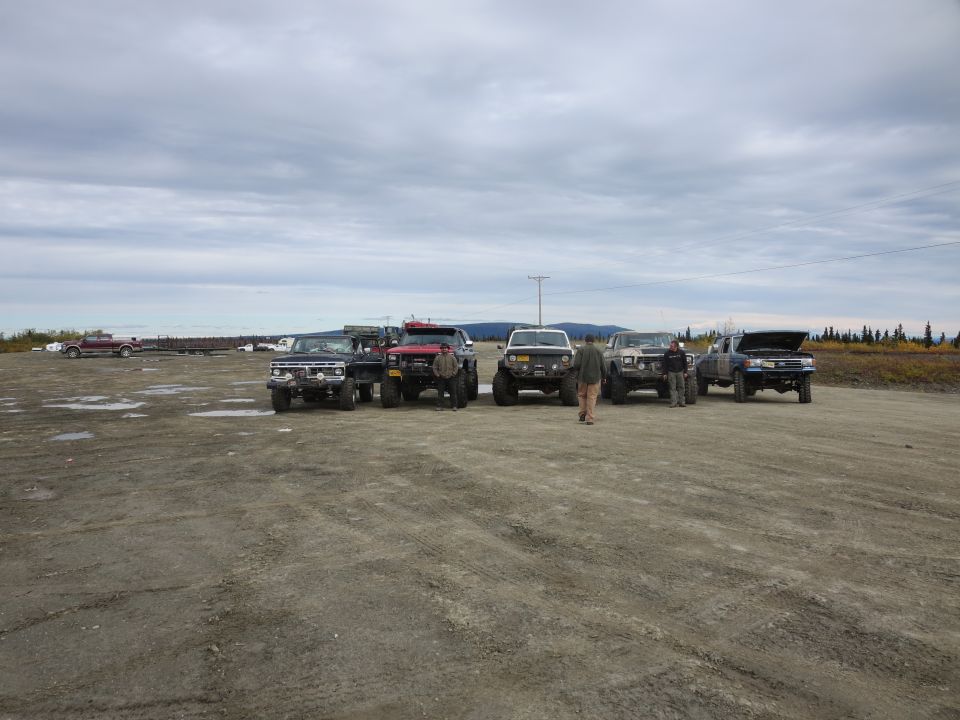 Group of lifted trucks parked in a dirt lot under a cloudy sky