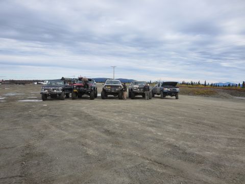 1990 Ford F-250 - Several off-road trucks are parked together in an outdoor lot with a treeline and mountains in the background.