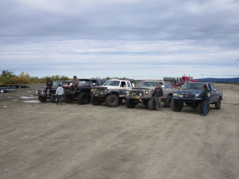 1990 Ford F-250 - A lineup of pickup trucks, including a 1990 Ford F-250, are parked in a dirt lot under a cloudy sky.