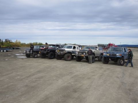 1990 Ford F-250 - A group of modified pickup trucks are parked together outdoors under a cloudy sky.