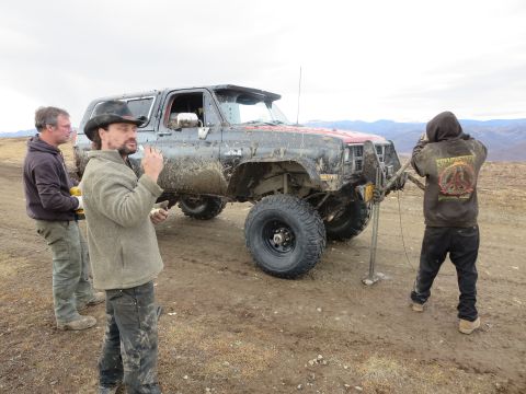 1990 Ford F-250 - Three people are gathered around a heavily modified and mud-covered SUV in an outdoor, off-road setting.