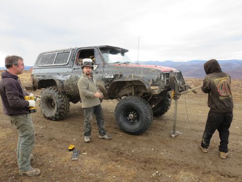 1990 Ford F-250 - A heavily modified SUV is being worked on by two men in a muddy, outdoor environment.