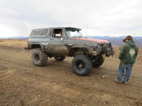 1990 Ford F-250 - A heavily modified, mud-covered SUV sits on a dirt track with a person standing nearby.