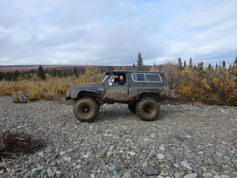 1990 Ford F-250 - A heavily modified SUV with large off-road tires sits on a gravel path with autumn foliage in the background.
