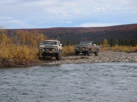 1990 Ford F-250 - Two older model pickup trucks are parked on the rocky bank of a river, with trees showing fall colors.