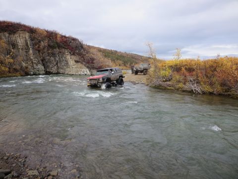 1990 Ford F-250 - Two off-road vehicles navigate a shallow river during autumn.