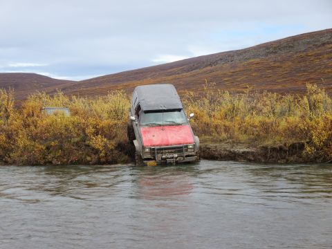 1990 Ford F-250 - This SUV with a 1990s-style grille is partially submerged in a river, navigating rough terrain.