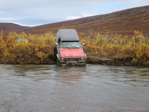 1990 Ford F-250 - An off-road vehicle is stuck in a river with autumn foliage in the background.