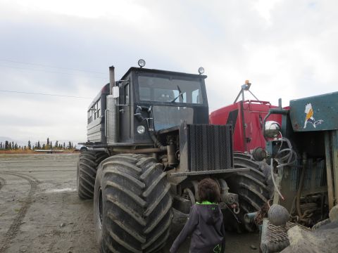 1990 Ford F-250 - A large tractor with oversized tires is parked next to a red trailer under an overcast sky.