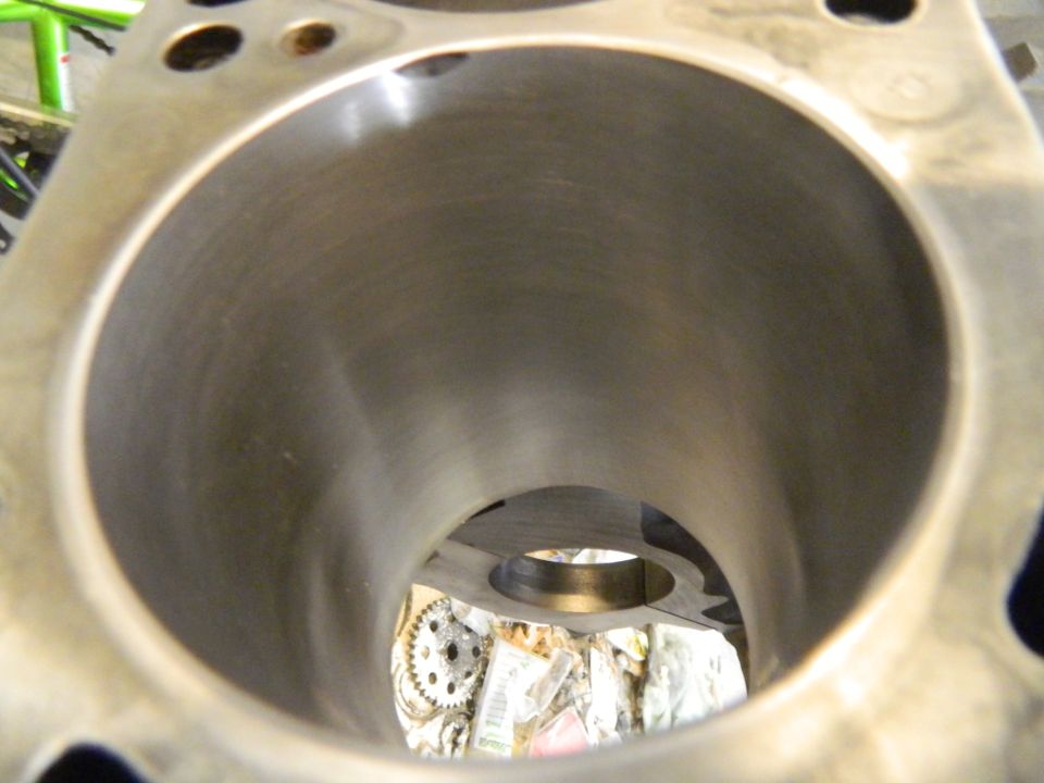 Engine cylinder interior with visible honing marks and a gear in the background