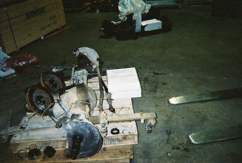 1983 Ford Bronco - Two vehicle axles are disassembled and resting on a wooden pallet in a warehouse setting.